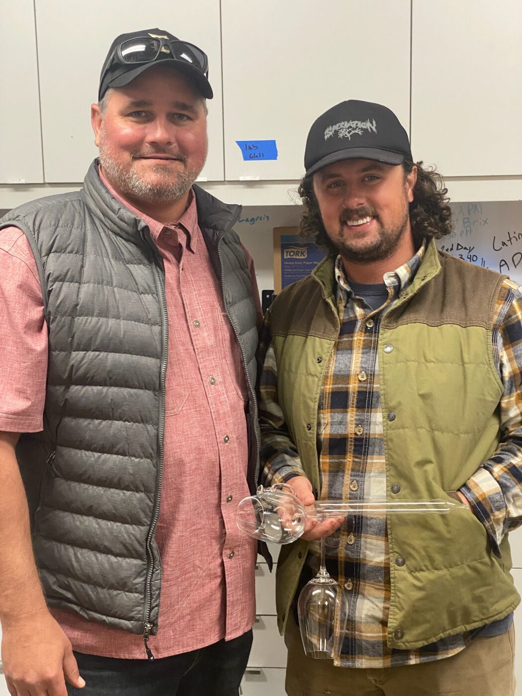Elegant image of two men celebrating the 2022 BOS Wine harvest, showcasing winemakers with wine glasses in a winery setting.
