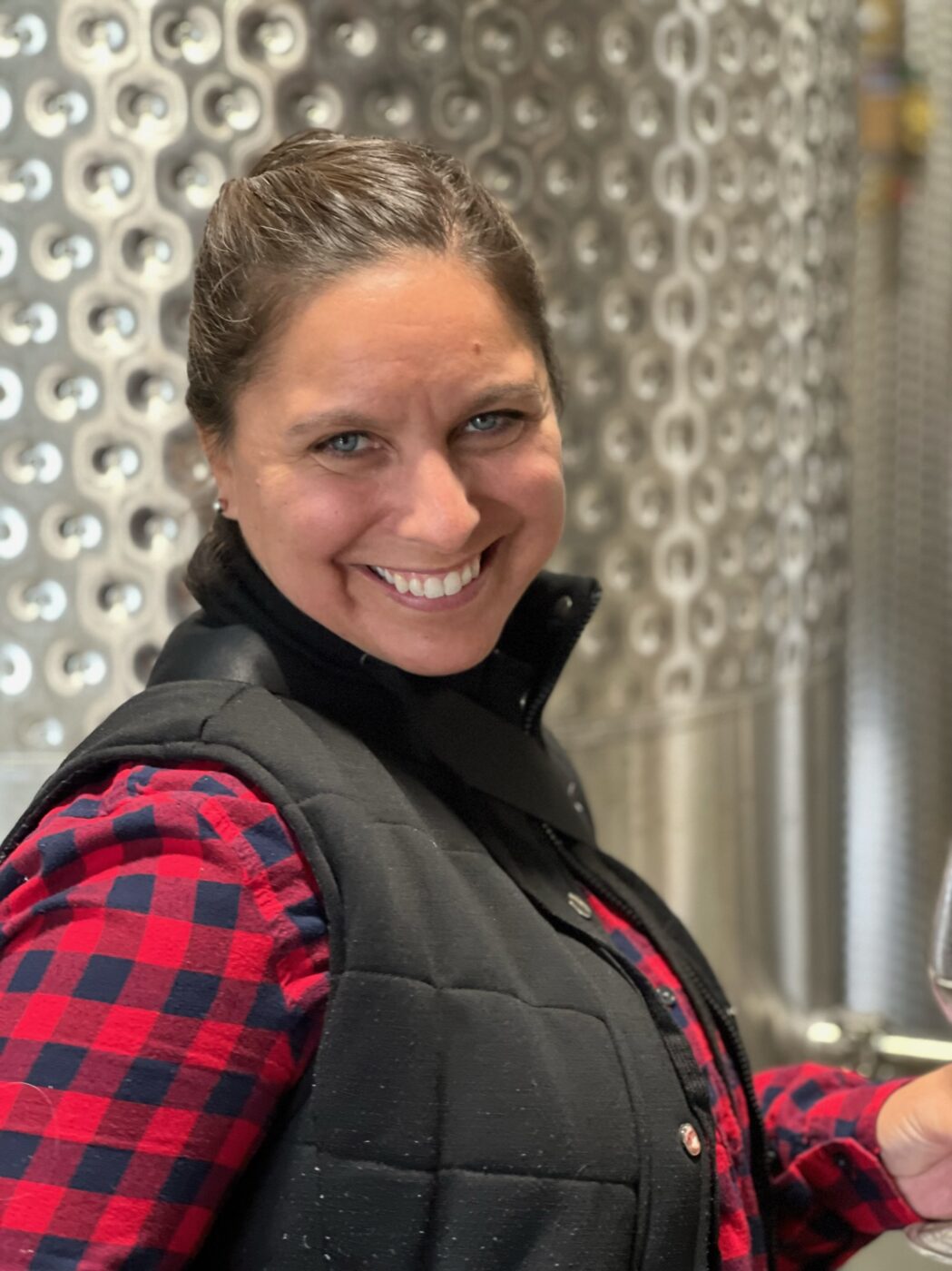 Woman smiling at winery tanks during harvest.