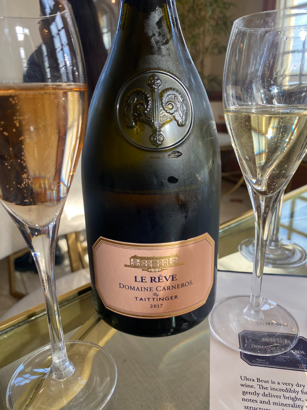 Elegant Domaine Carneros Taittinger 2017 sparkling wine bottle with glasses of champagne on a table.